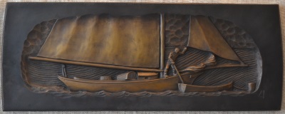 Photo of a bronze casting of a bas-relief carving of a sloop flying a luffing jib and mainsail, with a sailor gaffing a moored dinghy.