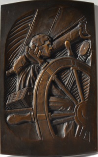 Photo of bronze casting of bas-relief carving of a man with curly hair at the wheel of a ship. A large boom secured by a block and tackle are behind his head.