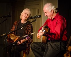 Photo of Cindy Mangsen playing a small accordion and Steve Gillette playing a guitar with microphones.
