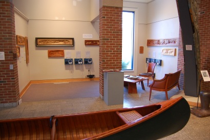 Photo of wood carvings in a gallery, with a cedar-ribbed canvas canoe in the foreground.